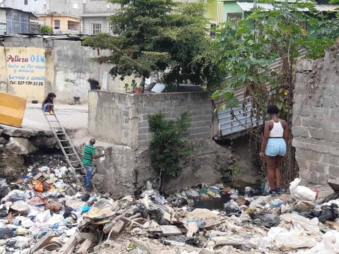 Moradores de Pantoja cruzan sobre la basura de una ca&ntilde;ada por falta de un puente