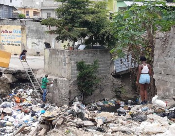 Moradores de Pantoja cruzan sobre la basura de una ca&ntilde;ada por falta de un puente